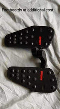 Pair of black rider footboards with raised grip points, shown as an optional accessory