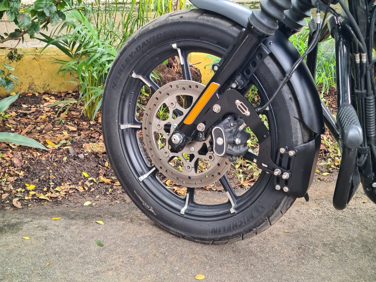 Close-up of the front mudslinger flap and metal mounting brackets beside the motorcycle's front wheel